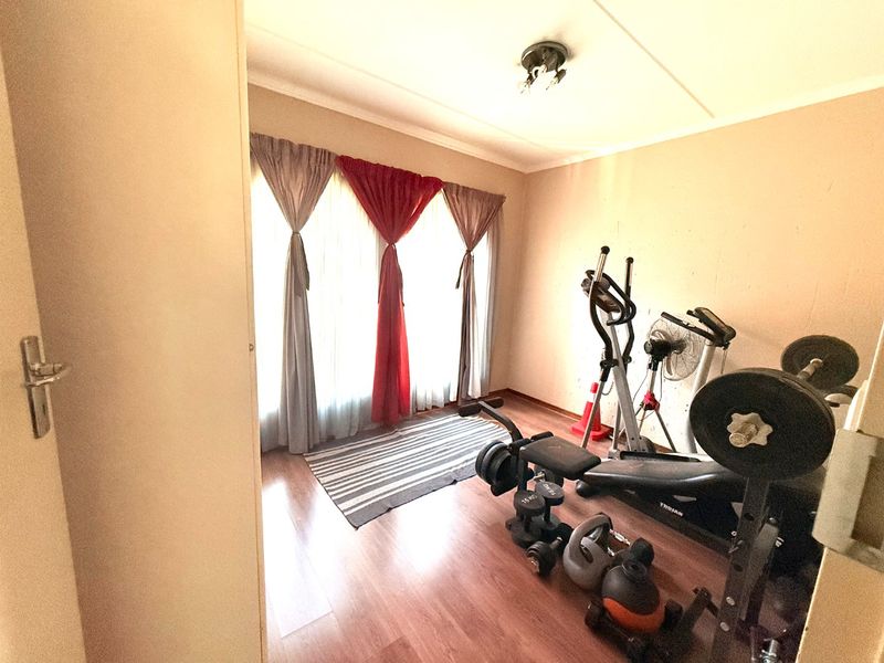 A functional room currently utilized as a home gym, featuring laminate flooring and natural light through large windows.