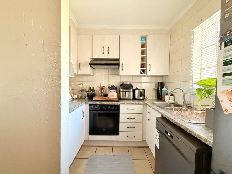 A functional galley-style kitchen featuring light-toned cabinetry, tiled backsplash, built-in oven with extractor fan, and durable tiled flooring.