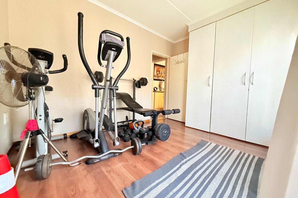 A bedroom currently utilized as a home gym, featuring laminate flooring and built-in cupboards.