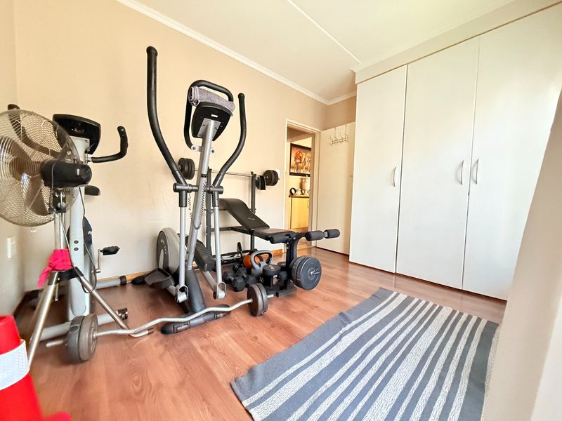 A bedroom currently utilized as a home gym, featuring laminate flooring and built-in cupboards.