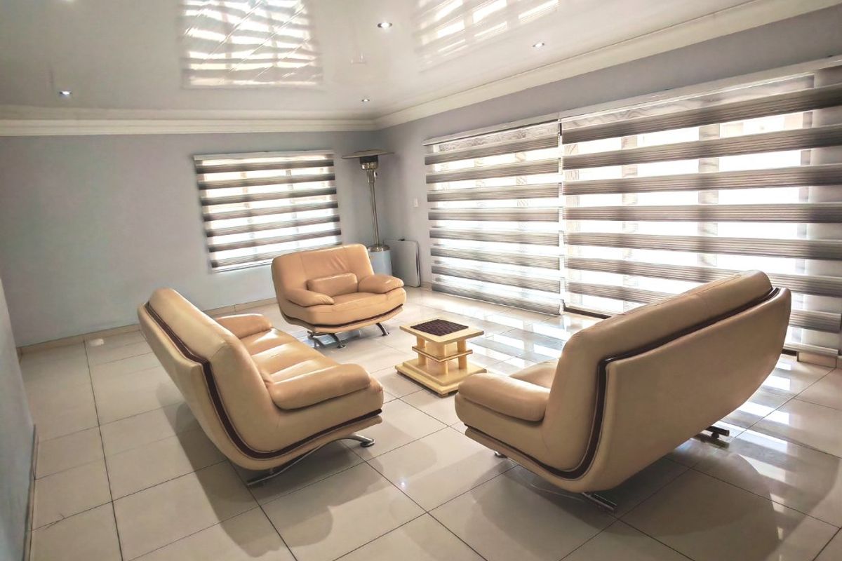 Spacious living room featuring glossy tiled flooring, recessed downlighting, and modern zebra blinds, creating a bright and contemporary atmosphere.