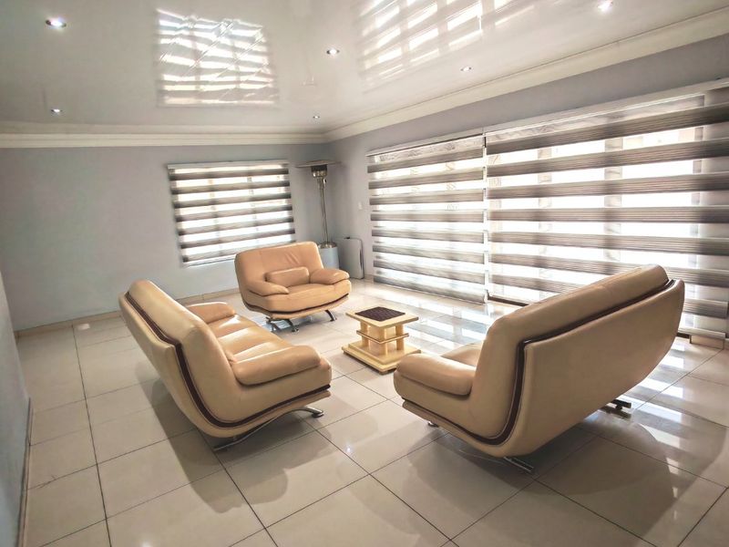 Spacious living room featuring glossy tiled flooring, recessed downlighting, and modern zebra blinds, creating a bright and contemporary atmosphere.