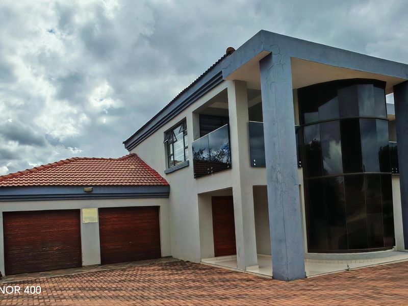 Modern double-story residence featuring a double garage, paved driveway, and a distinctive curved glass facade with an upper-level balcony.