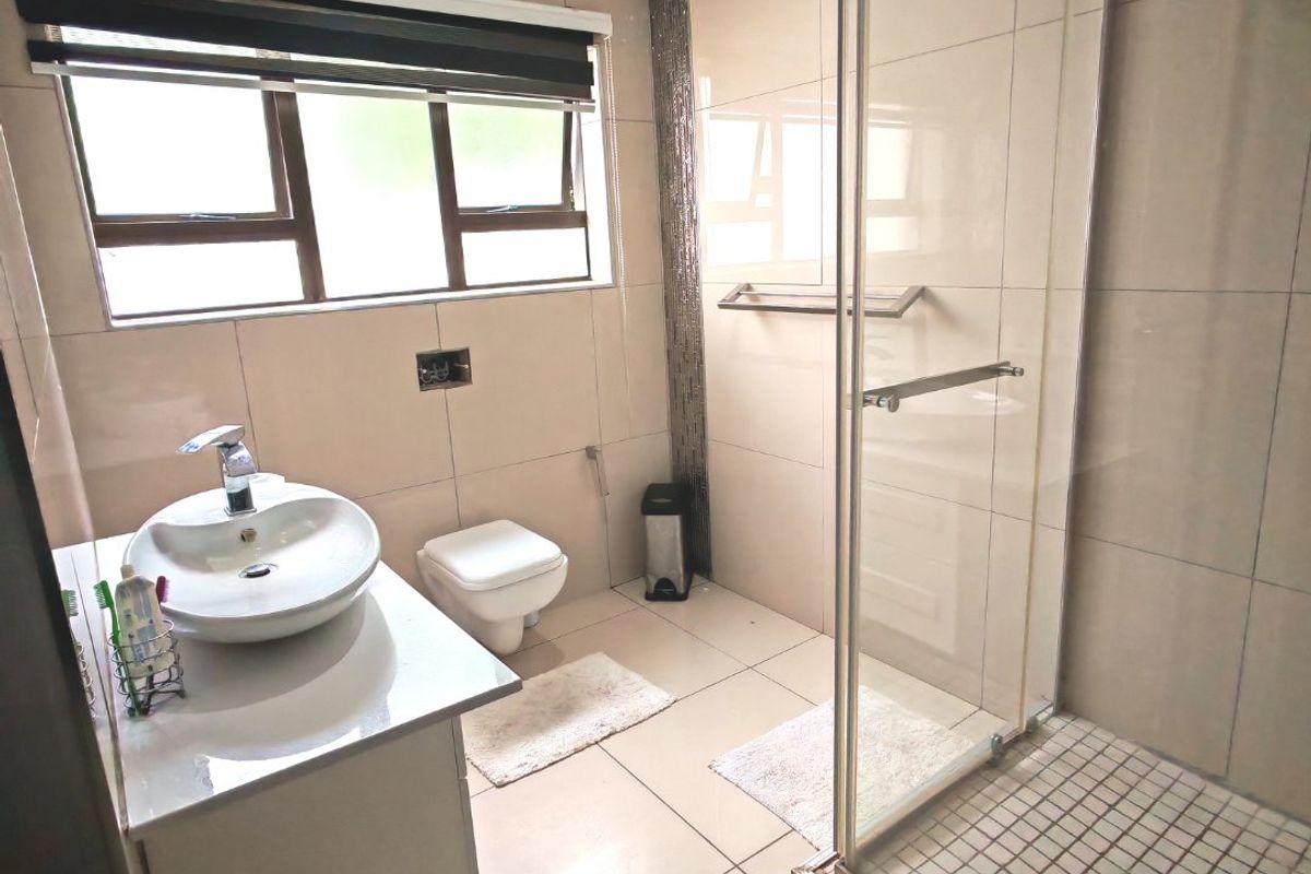 Modern bathroom featuring a vessel sink vanity, wall-mounted toilet, and a glass-enclosed shower with tiled flooring.