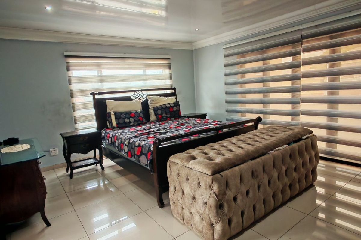 Spacious bedroom featuring glossy ceiling finish, large tiled flooring, and modern dual-layer roller blinds providing adjustable natural light.