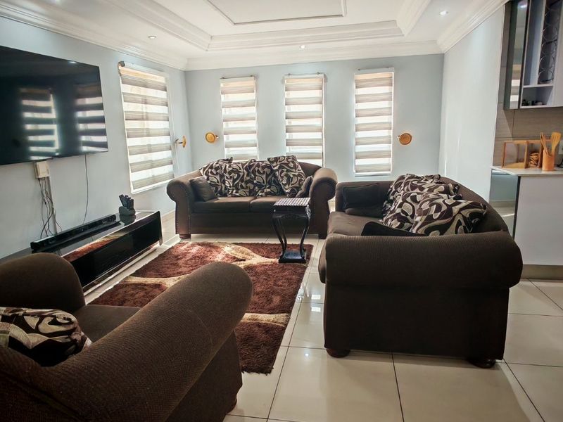 An open-plan living area featuring tiled flooring, recessed ceiling details, and modern roller blinds, creating a bright and functional space.