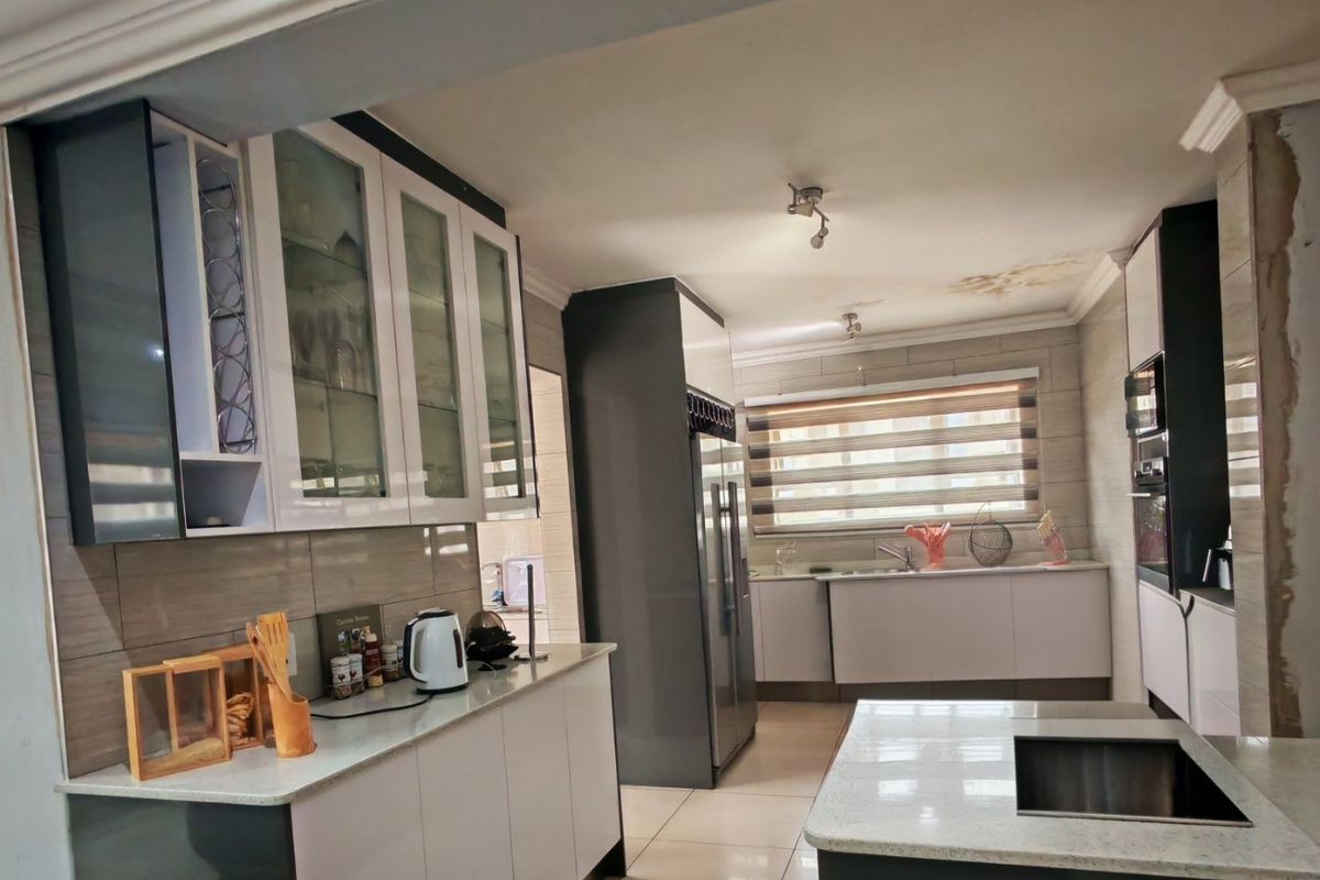 Modern kitchen featuring two-tone cabinetry, stone countertops, a central island with sink, and built-in appliances, though ceiling shows signs of water damage.