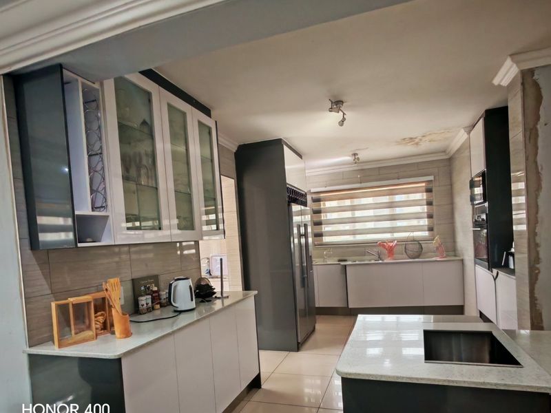 Modern kitchen featuring two-tone cabinetry, stone countertops, a central island with sink, and built-in appliances, though ceiling shows signs of water damage.