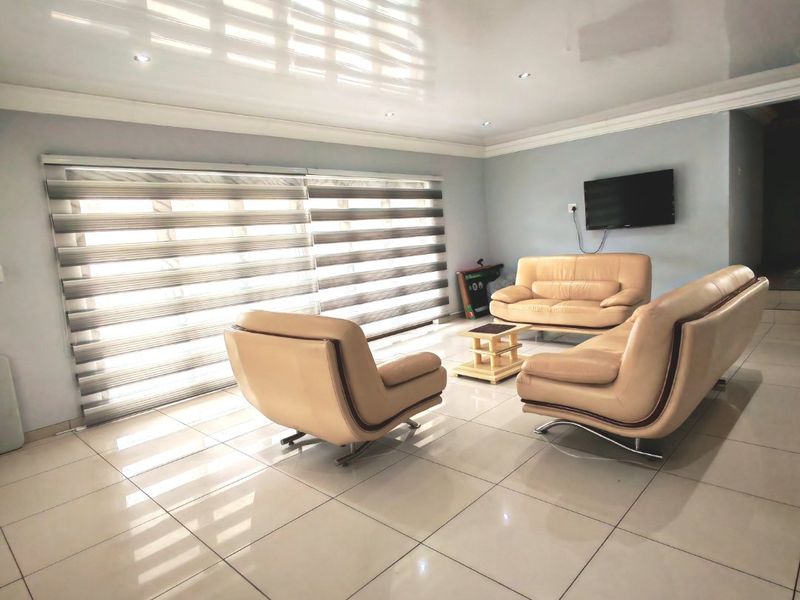 Spacious living room featuring large format floor tiles, a glossy ceiling finish, and modern zebra blinds providing ample natural light.