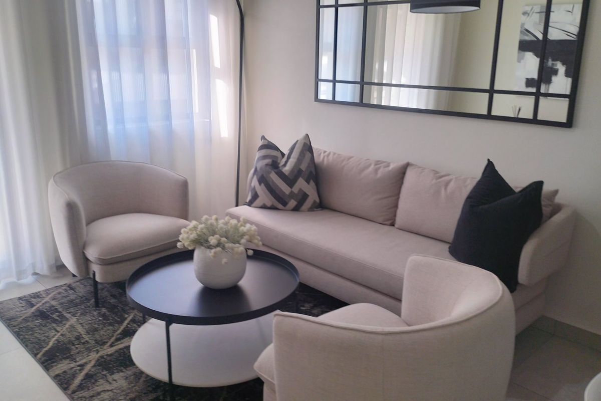 A well-lit living room featuring neutral tones, tiled flooring, and a large decorative wall mirror, creating a bright and inviting atmosphere.