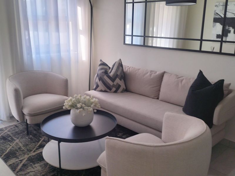 A well-lit living room featuring neutral tones, tiled flooring, and a large decorative wall mirror, creating a bright and inviting atmosphere.
