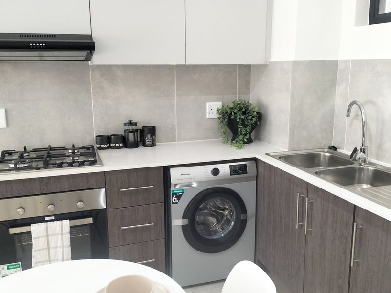 Modern kitchen featuring sleek grey cabinetry, stone countertops, a built-in gas hob, oven, extractor fan, and an integrated washing machine.
