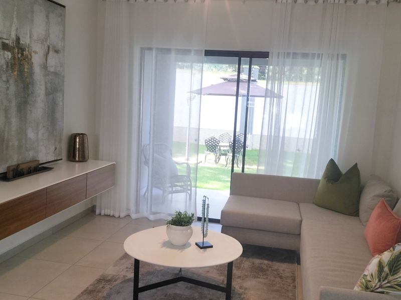 A bright living room featuring large sliding glass doors that open onto a private patio and garden area, creating a seamless indoor-outdoor flow.