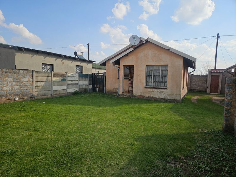 Rear view of a detached house featuring a lawn, precast concrete boundary walls, and security features on windows and doors.