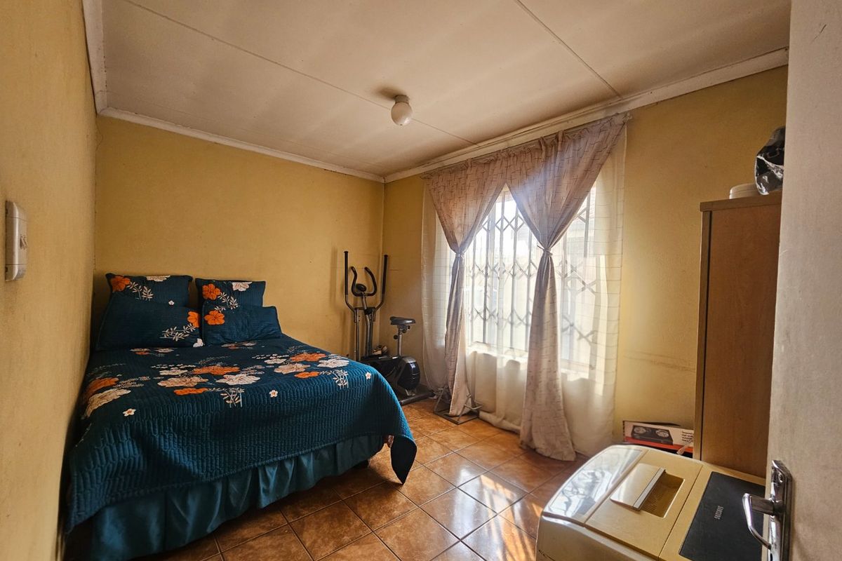 A bedroom featuring tiled flooring and a window with a security gate, requiring cosmetic updates to improve the overall aesthetic.