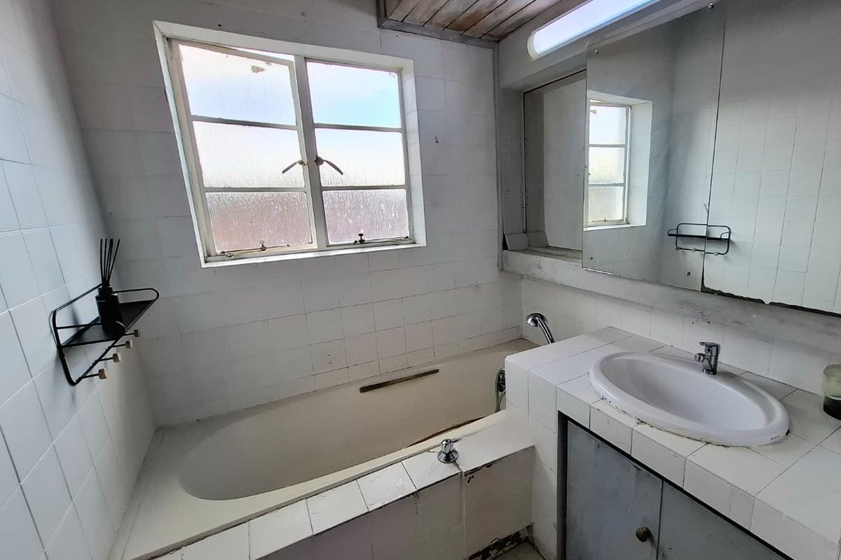 A dated bathroom featuring a built-in bathtub, tiled vanity with integrated basin, and wall-mounted mirror, requiring renovation to update finishes and fixtures.