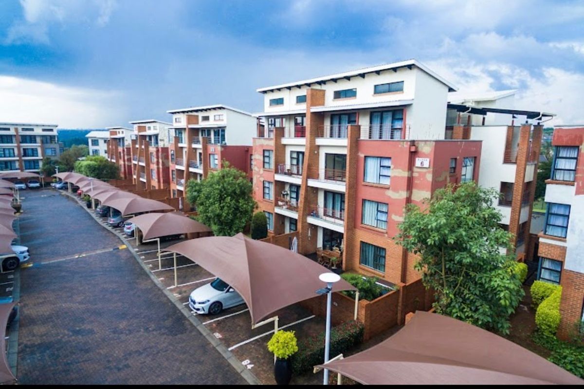 Aerial view of a multi-story apartment complex featuring paved parking areas with shade cloth carports and brick-accented building facades.