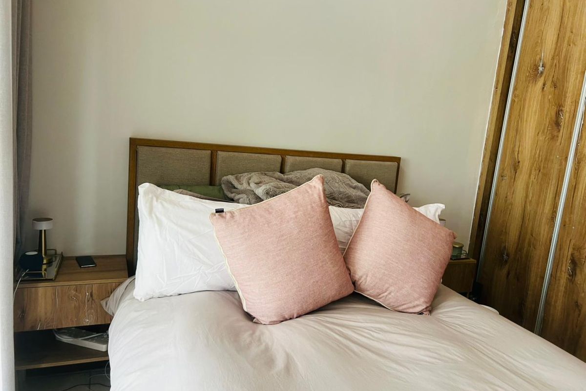 A cozy bedroom featuring a neutral upholstered headboard and a functional built-in wooden wardrobe with sliding doors.