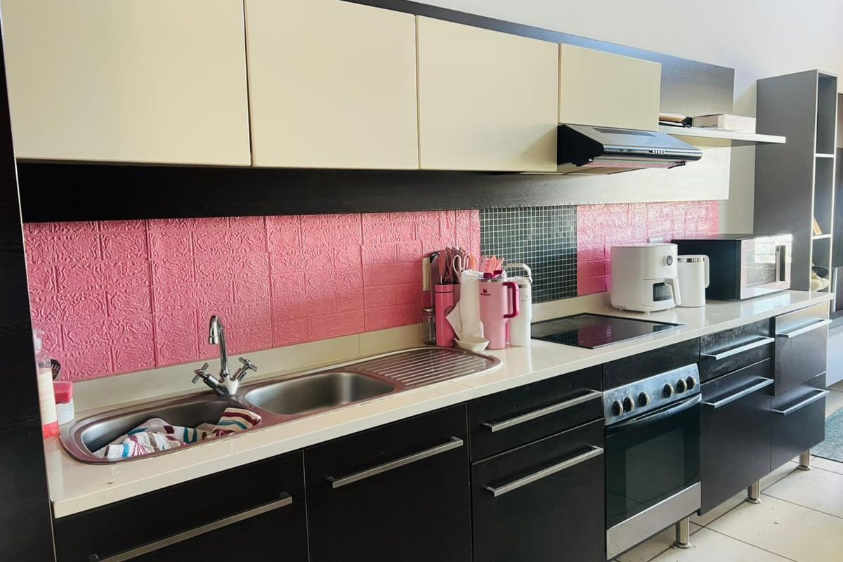 A functional kitchen featuring dark lower cabinetry, light upper cabinets, a stainless steel sink, and an integrated electric hob with an extractor fan.