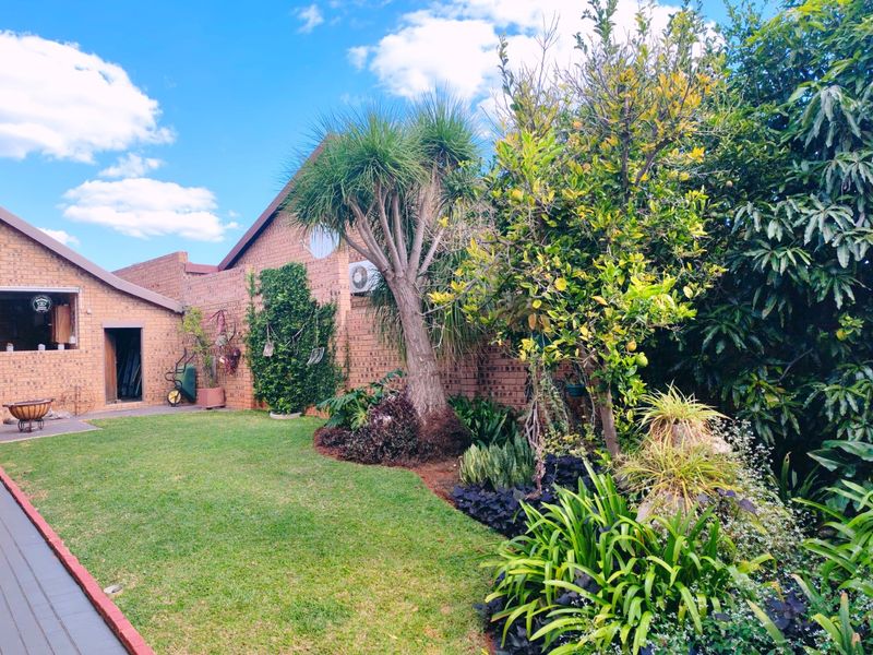 A well-maintained rear garden featuring a brick facade, paved walkway, and established landscaping with a brick chimney and boundary wall.