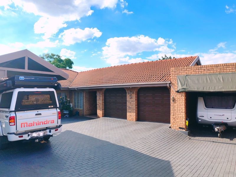 Front exterior view featuring a paved driveway, double garage, and additional covered parking structures with brick facade and tiled roofing.