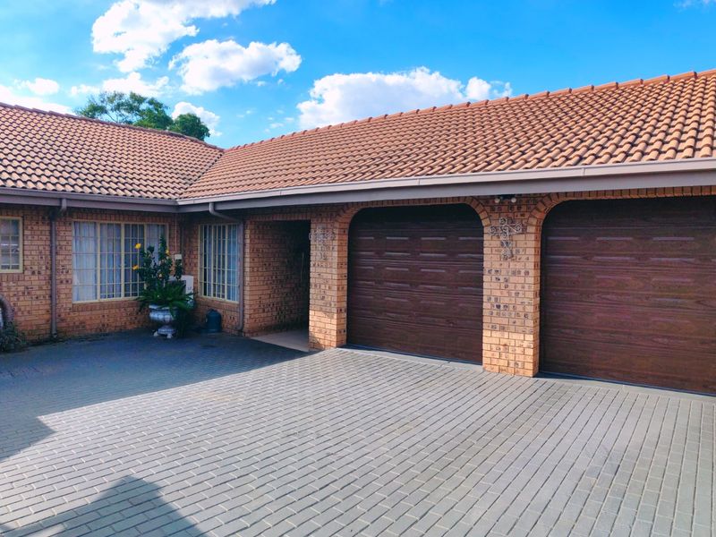 Front exterior view of a brick house featuring a double garage with brown sectional doors and a paved driveway.