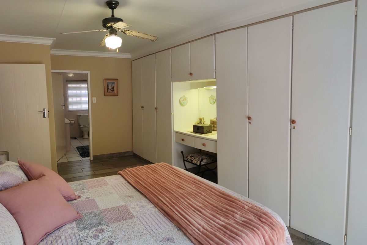 Bedroom featuring extensive built-in cupboards with an integrated vanity area, ceiling fan, and tiled flooring, with an adjoining bathroom visible.