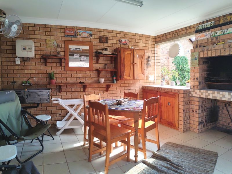 Covered patio area featuring a built-in brick braai, tiled flooring, and integrated cabinetry with a sink, suitable for outdoor entertaining.