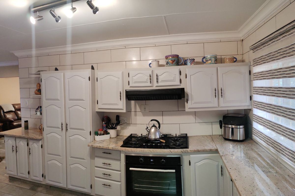 A functional kitchen featuring white cabinetry, granite countertops, a gas hob with extractor fan, and a tiled backsplash.