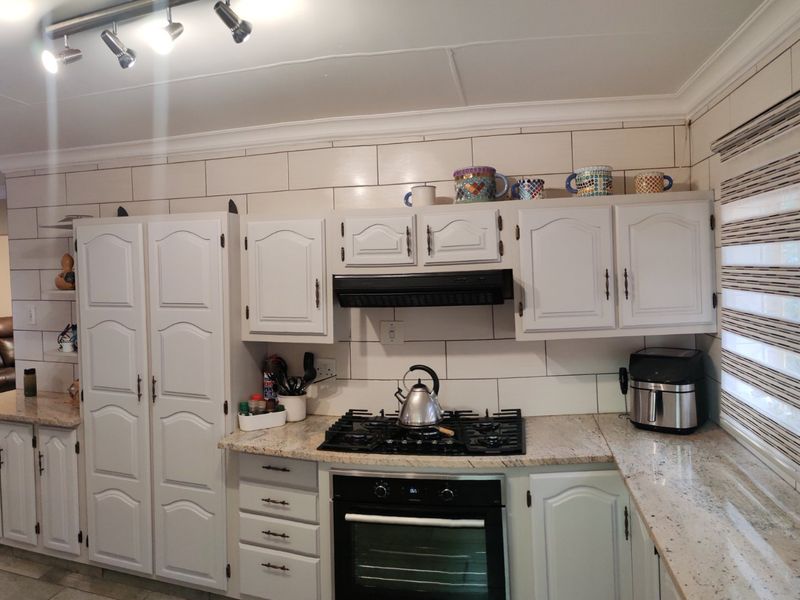 A functional kitchen featuring white cabinetry, granite countertops, a gas hob with extractor fan, and a tiled backsplash.
