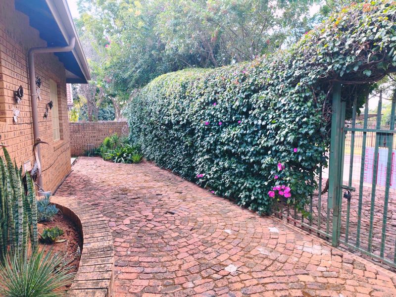 A side entrance area featuring brick paving, a curved brick retaining wall, and a metal gate covered by a mature climbing hedge.