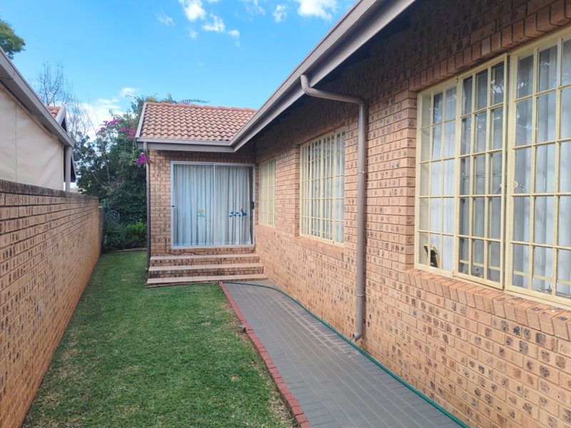 Rear exterior view of the house featuring face brick walls, a tiled roof, a paved walkway, and a sliding door leading to the garden.