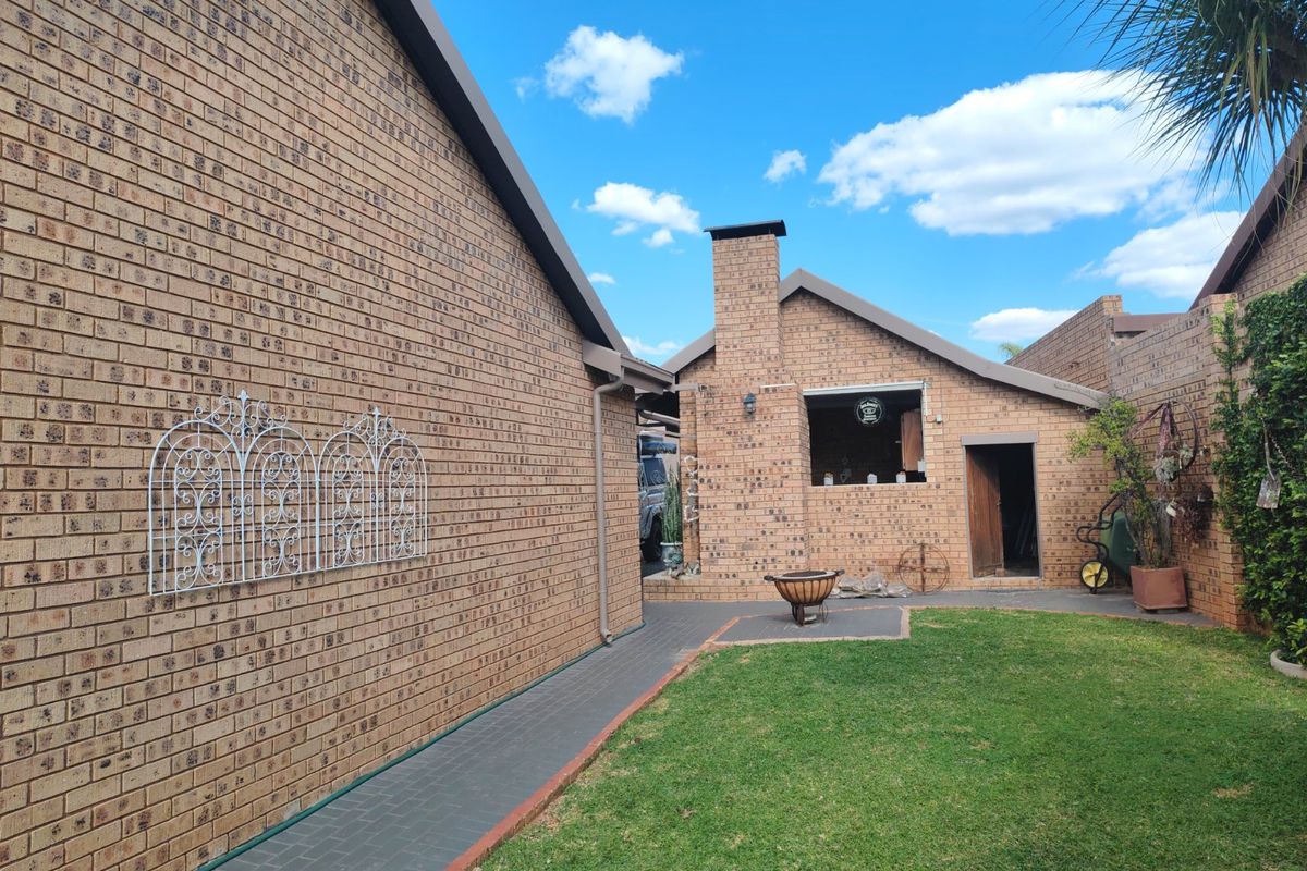 Rear exterior view of the property featuring a face brick facade, paved walkway, lawn area, and a built-in outdoor fireplace.