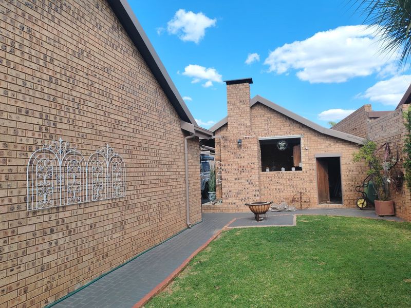 Rear exterior view of the property featuring a face brick facade, paved walkway, lawn area, and a built-in outdoor fireplace.
