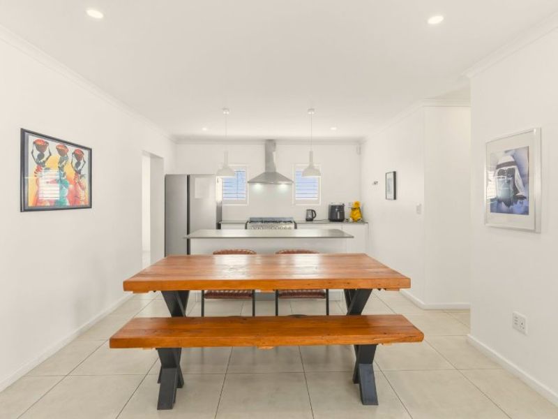 An open-plan kitchen and dining area featuring a central island, modern extractor fan, gas cooktop, and neutral tiled flooring throughout.