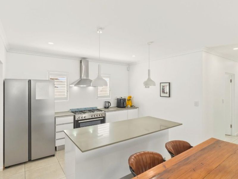 Modern kitchen featuring a central island with stone countertops, stainless steel gas stove, extractor fan, and sleek white cabinetry with tiled flooring.