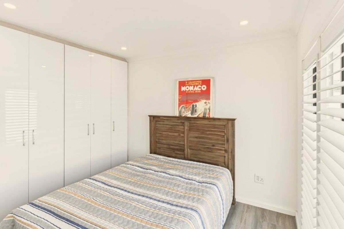 A bright and well-maintained bedroom featuring built-in white wardrobes, recessed downlighting, and modern laminate flooring with adjustable venetian blinds.