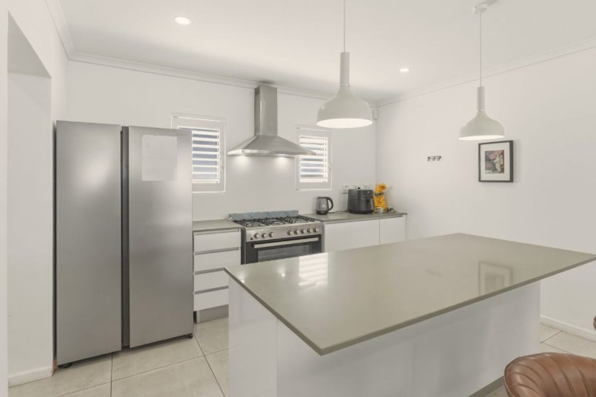 Modern kitchen featuring a central island with stone benchtops, gas cooktop, stainless steel appliances, and stylish pendant lighting.
