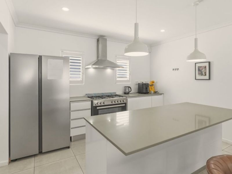 Modern kitchen featuring a central island with stone benchtops, gas cooktop, stainless steel appliances, and stylish pendant lighting.