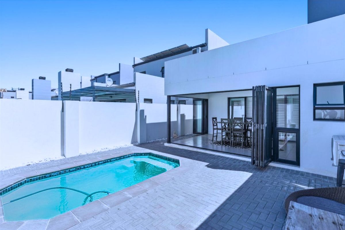 Rear exterior view featuring a private swimming pool, paved patio area, and modern stacking doors leading into the home.