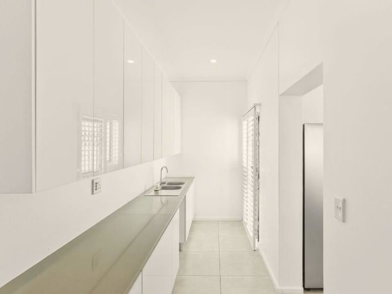 A clean, modern scullery featuring white high-gloss cabinetry, a stainless steel sink, and neutral tiled flooring.