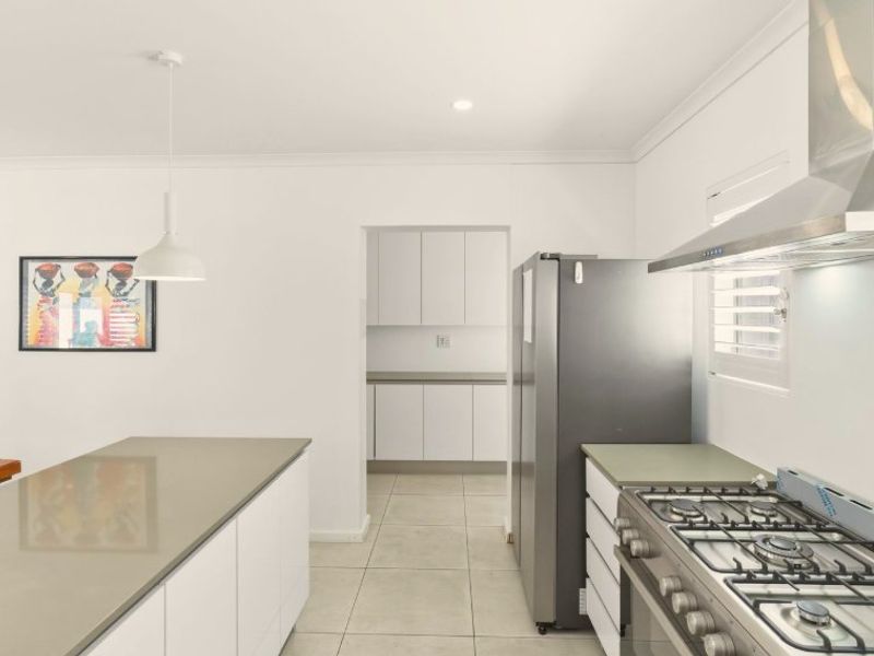 Modern kitchen featuring a central island with stone countertops, gas cooktop, stainless steel extractor fan, and clean white cabinetry with tiled flooring.