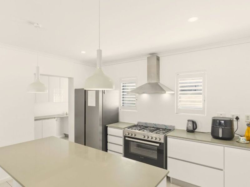 Modern kitchen featuring a central island, stone countertops, gas cooktop with stainless steel extractor, and clean white cabinetry with integrated lighting.