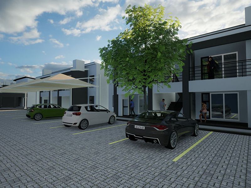 Modern residential complex exterior featuring paved parking area, shade sail structures, and upper-level balconies.