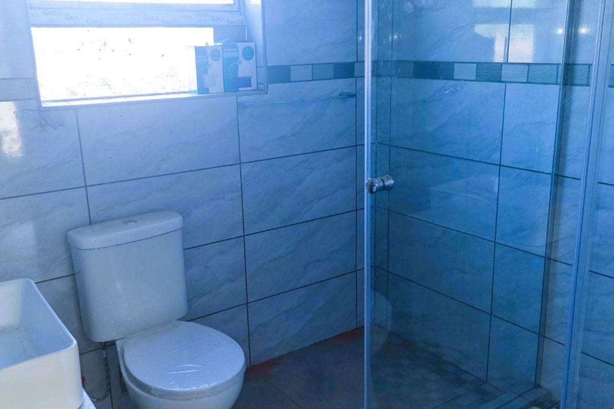 A functional bathroom featuring a glass shower enclosure, toilet, and vanity basin with tiled walls and flooring.