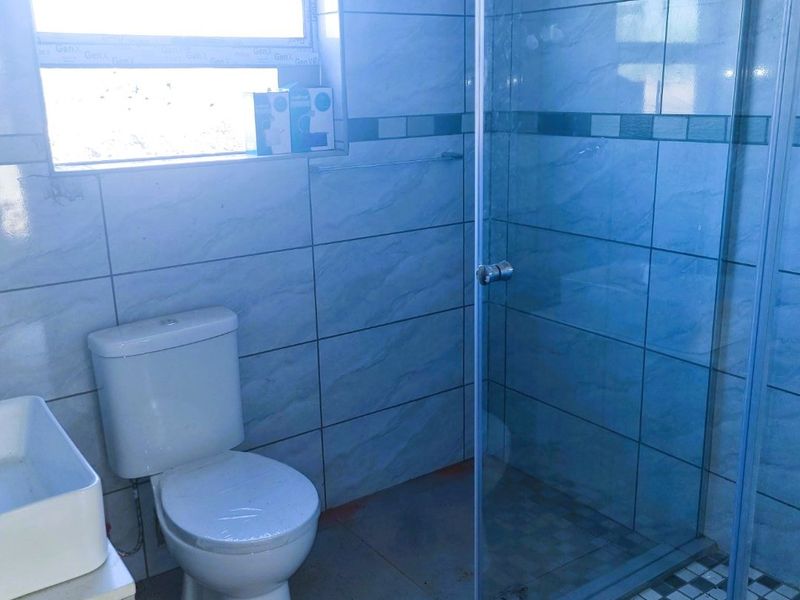 A functional bathroom featuring a glass shower enclosure, toilet, and vanity basin with tiled walls and flooring.