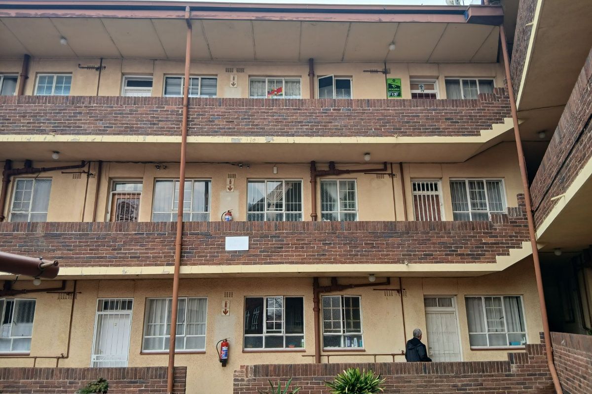 Exterior view of a multi-story apartment building featuring brick facade, metal window frames, and external drainage infrastructure.