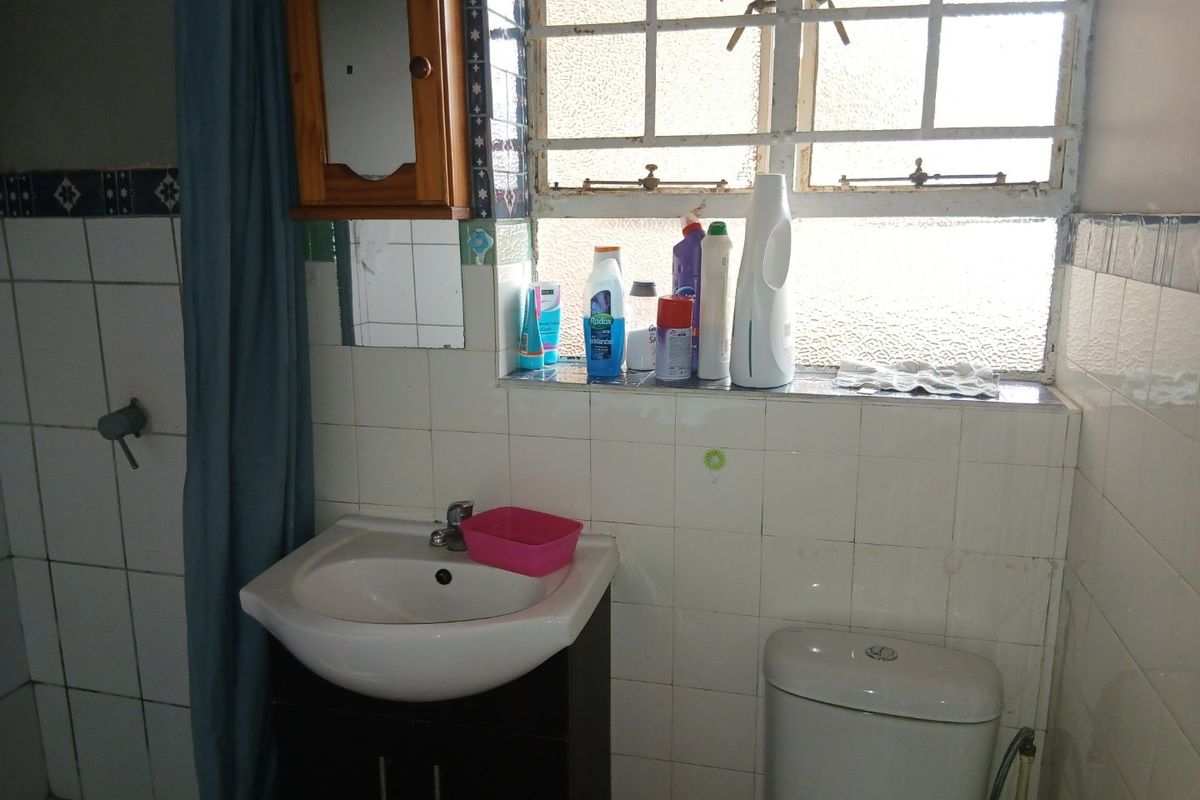 A functional bathroom featuring a pedestal washbasin with vanity, toilet, and tiled walls, requiring cosmetic updates to modernize the space.