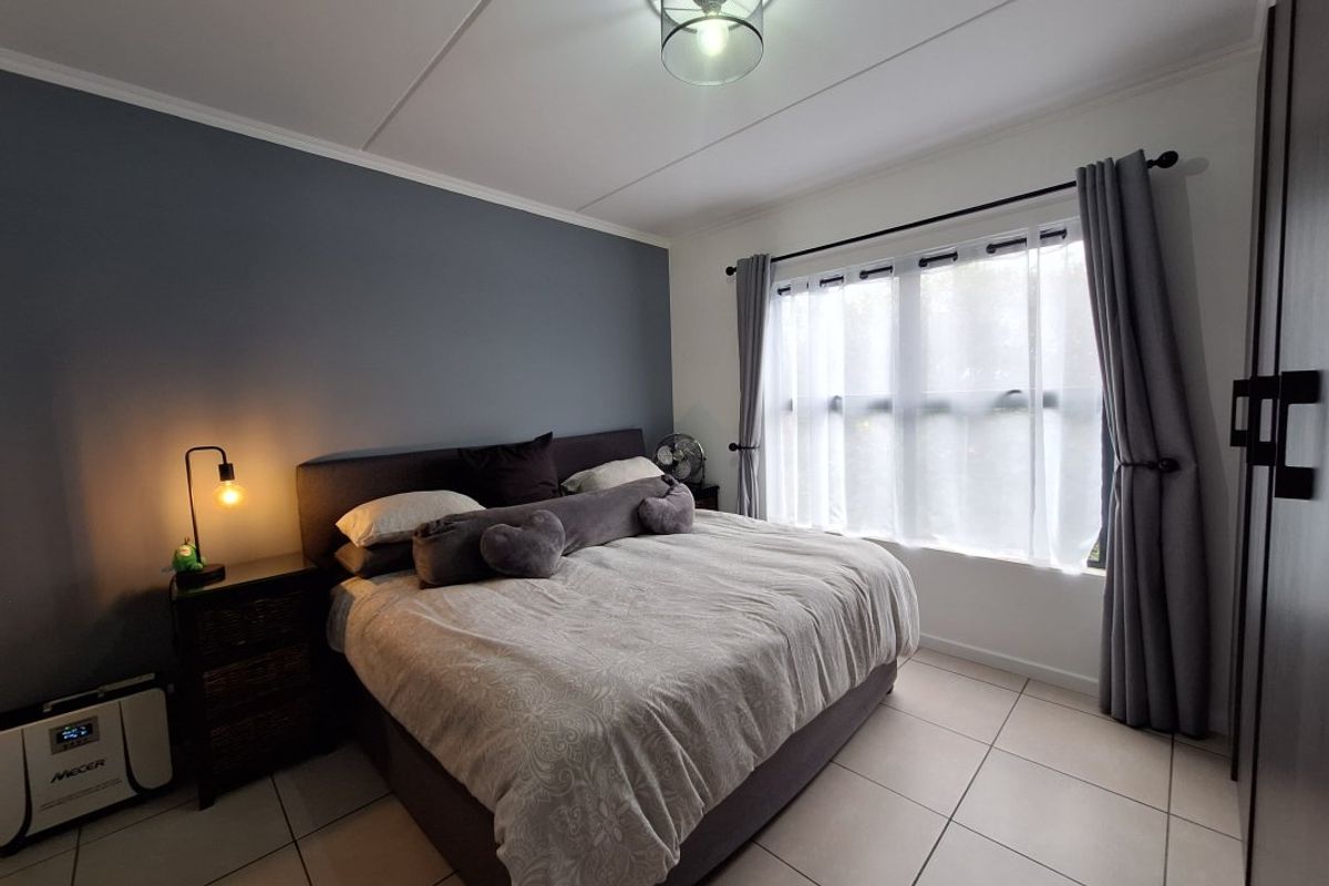 A well-maintained bedroom featuring neutral tiled flooring, a feature wall, and built-in wardrobe storage with ample natural light.