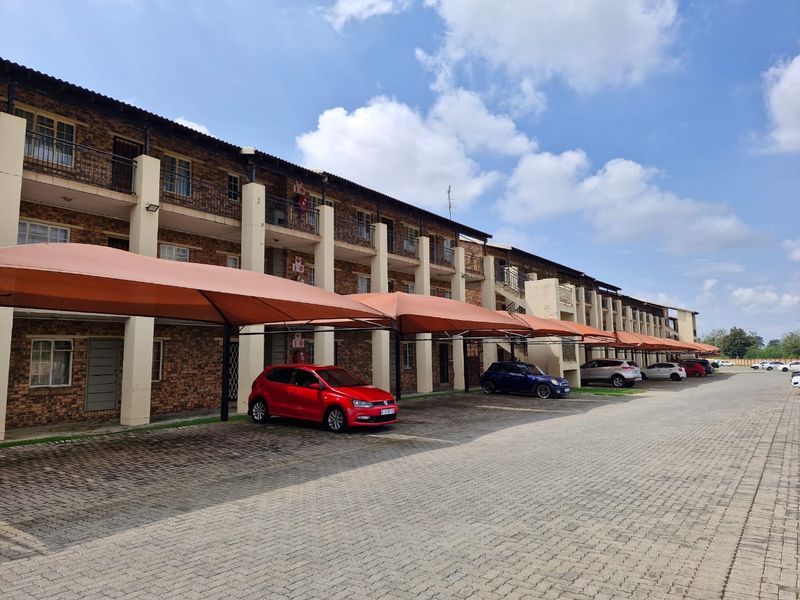 Exterior view of a multi-story apartment complex featuring brick facade, private balconies, and covered parking bays for residents.
